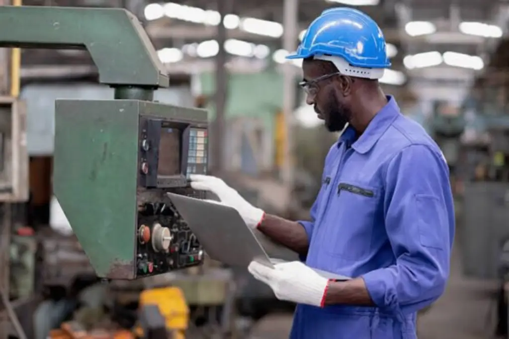 Worker in a hard hat checking a machine control panel in a molding shop